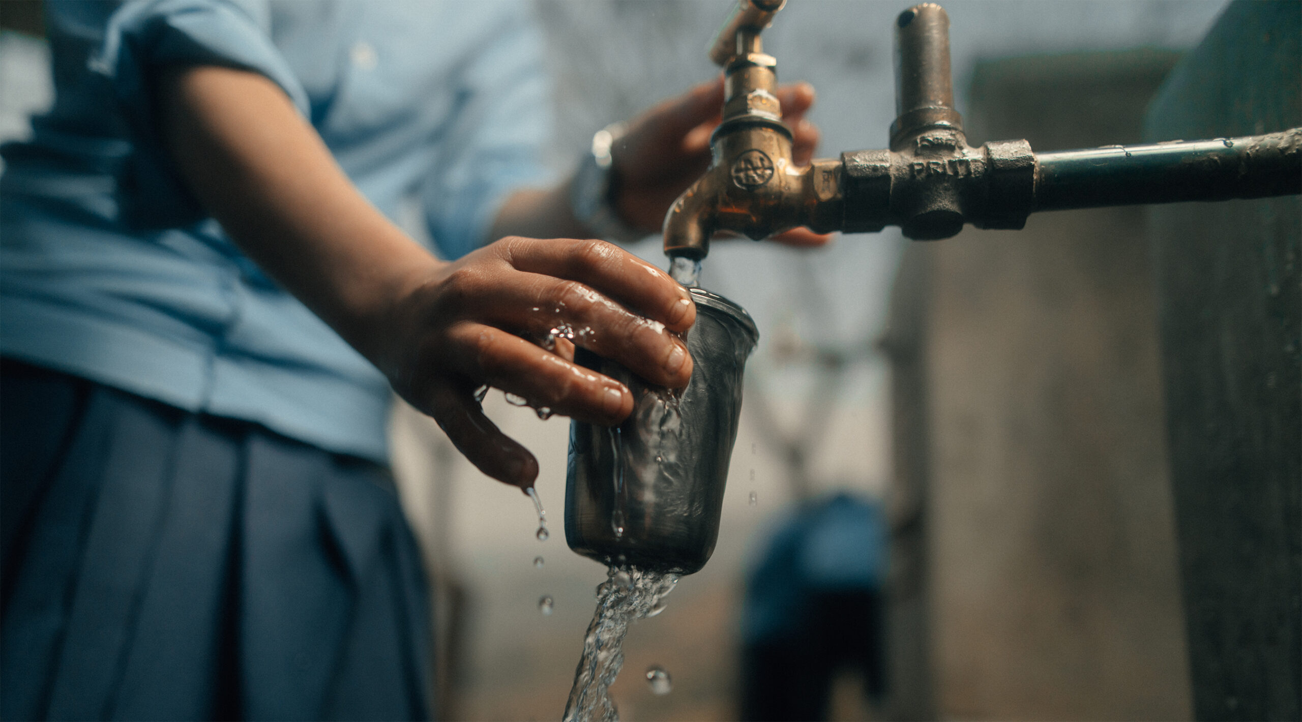 girls hand holding a cup overflowing with water from a spigot from a Charity Water water project